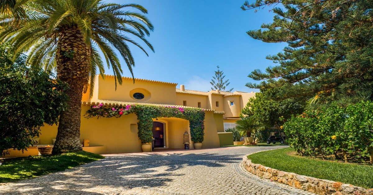 Vila Joya entrance with bougainvillea arch and palm trees above Galé